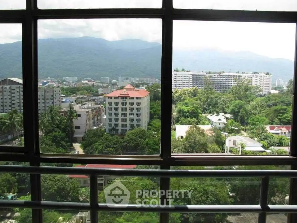 Stunning cityscape view from a high-rise window overlooking lush greenery and distant mountains.