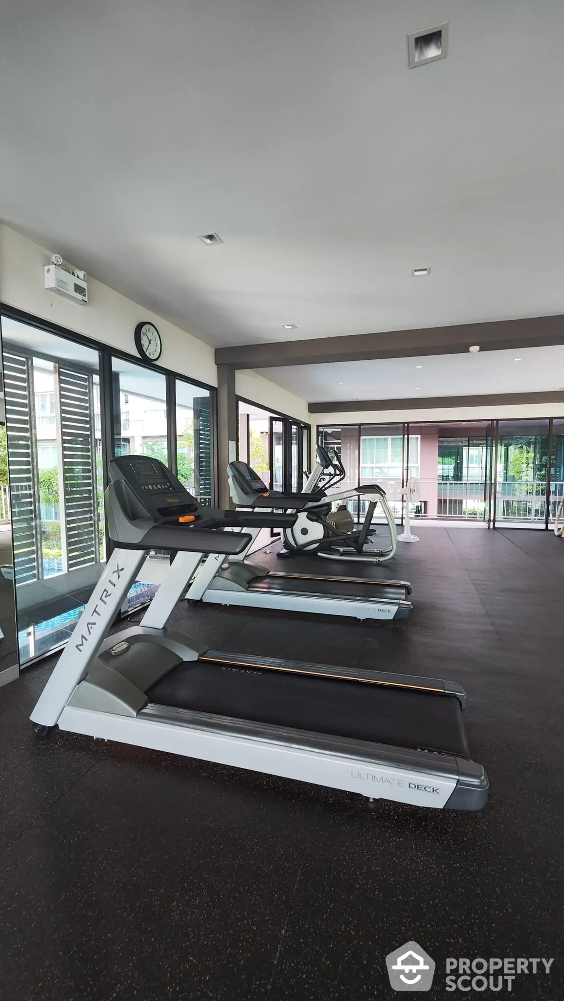 Modern gym facility in a residential building with state-of-the-art treadmills, ample lighting, and a view of the pool area, perfect for fitness enthusiasts.