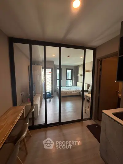 Modern apartment interior with glass partition separating living area and bedroom, featuring sleek furniture.