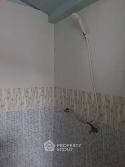 Simple bathroom with showerhead and tiled walls, ideal for compact living spaces.