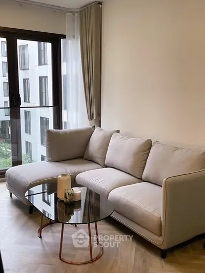 Modern living room with stylish sofa and glass coffee table near large window.