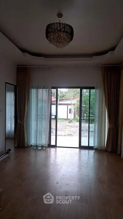 Spacious living room with elegant chandelier and large glass doors opening to garden view.