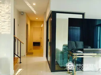 Modern living room with sleek design and large TV, featuring glass doors and bright lighting.