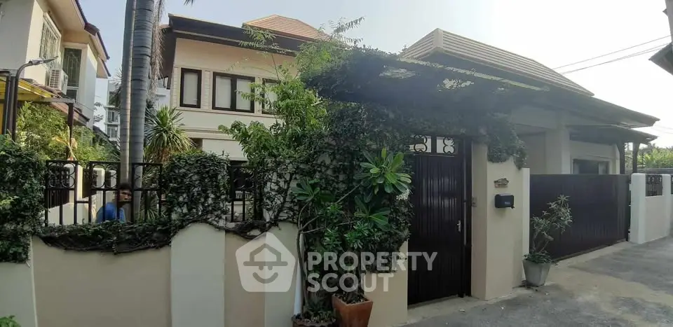 Charming two-story house with lush greenery and secure gated entrance in a serene neighborhood.