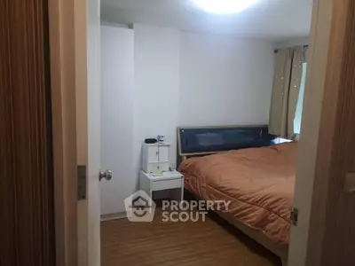 Cozy bedroom with wooden flooring and modern furnishings in a well-lit apartment.