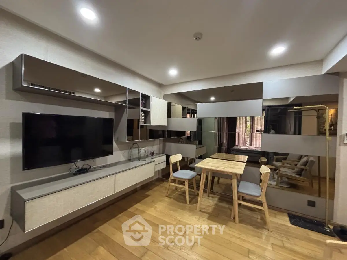 Modern living room with sleek furniture and wooden flooring, featuring a wall-mounted TV and stylish dining area.