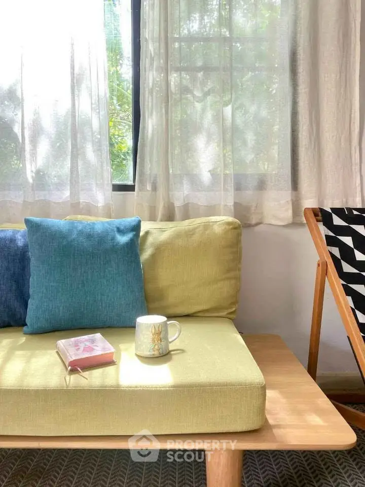 Cozy living room with stylish sofa, cushions, and natural light through sheer curtains.