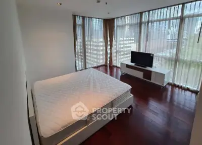 Spacious bedroom with large windows and city view, featuring a modern bed and sleek TV stand.