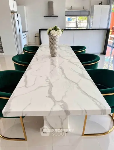 Luxurious modern kitchen with elegant marble dining table and plush green chairs.