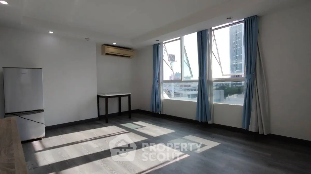 Spacious sunlit room with modern flooring and large windows in urban apartment.