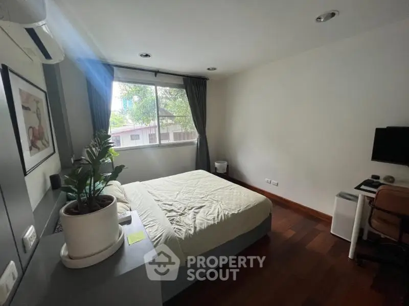 Cozy bedroom with wooden flooring, large window, and modern decor in a serene residential setting.