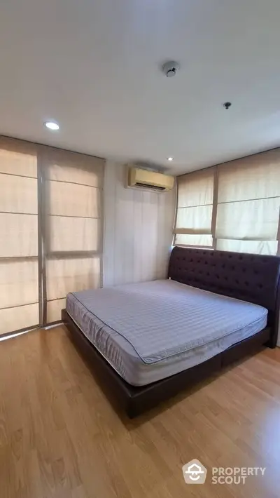 Spacious bedroom with polished wooden flooring, a large comfortable bed, and ample natural light filtering through elegant window shades.