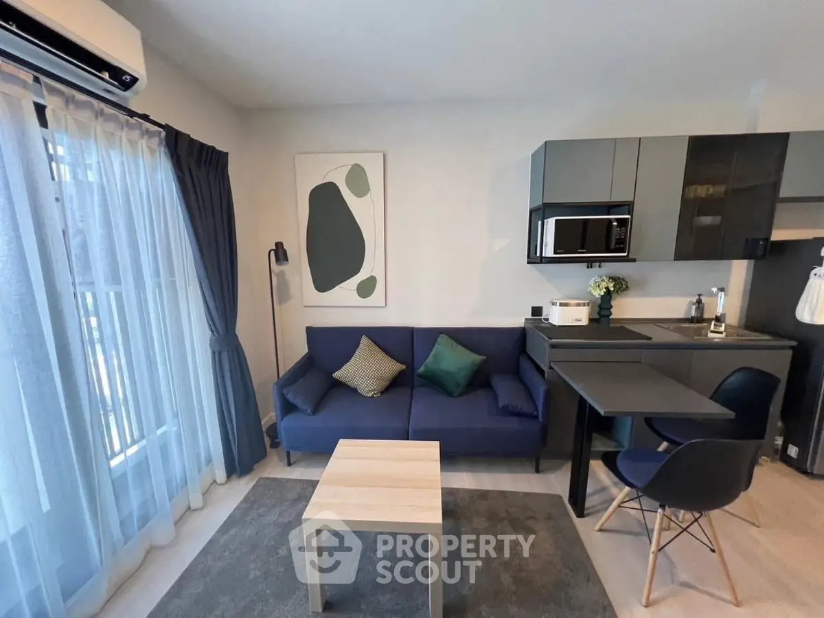 Modern living room with open kitchen, featuring sleek furniture and natural light.