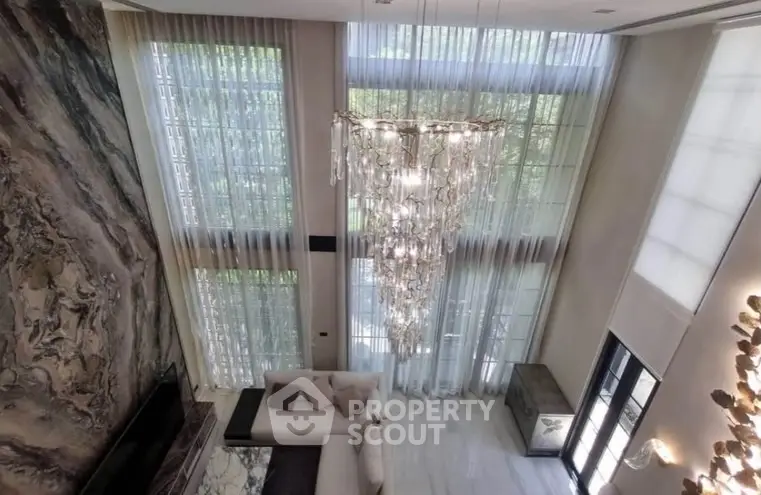 Luxurious high-ceiling living room with elegant chandelier and floor-to-ceiling windows.