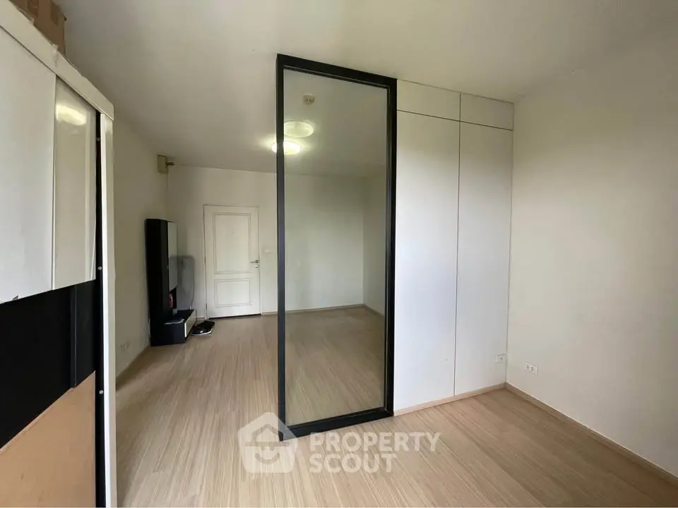 Spacious empty room with wooden flooring and large mirror, ideal for customization.