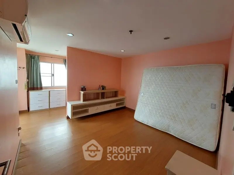 Spacious bedroom with wooden flooring and natural light, featuring a mattress and storage units.