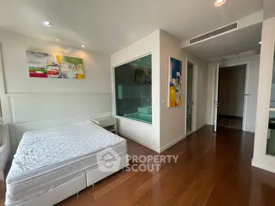 Modern bedroom with wooden flooring and abstract art, featuring a large window and cozy ambiance.