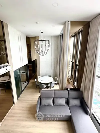 Modern living room with high ceilings and large windows, featuring a stylish chandelier and cozy seating area.