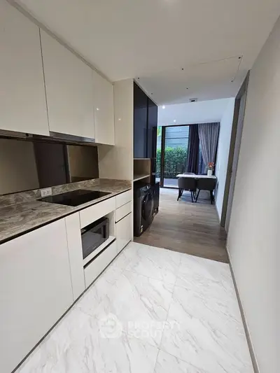 Modern kitchen with sleek cabinetry and integrated appliances leading to a cozy dining area with garden view.