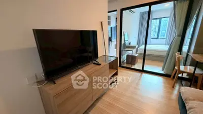 Modern apartment interior with sleek TV unit and glass partition leading to a cozy bedroom.