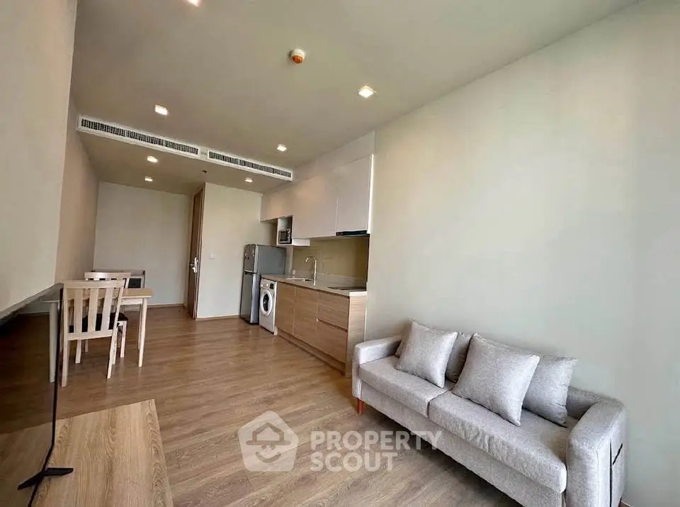 Modern open-plan living room with kitchen and dining area, featuring wooden flooring and neutral decor.