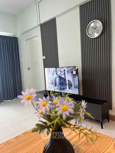 Modern living room with stylish decor and wall-mounted TV, featuring elegant floral arrangement.