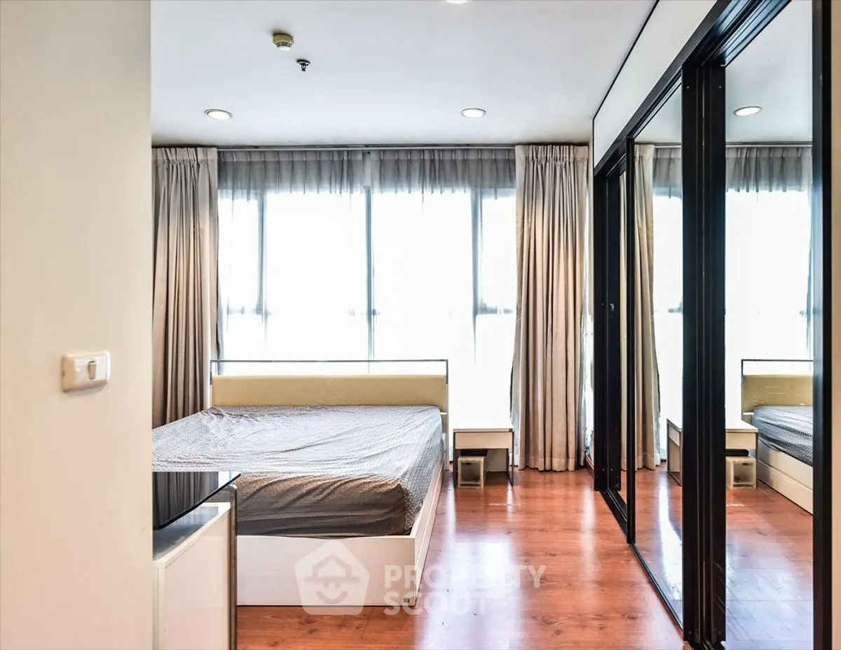 Spacious bedroom with large windows and mirrored closet doors, featuring elegant wooden flooring.