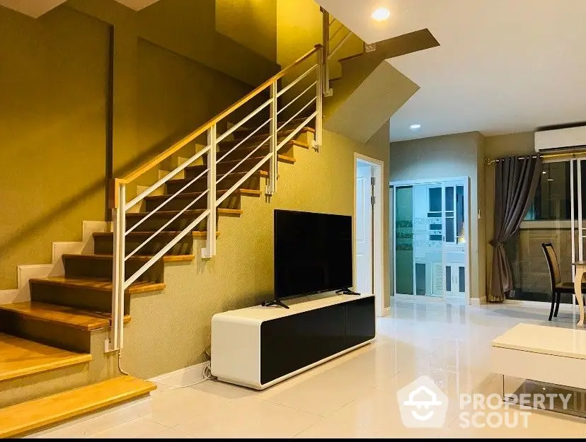 Spacious living room with high ceiling, modern staircase, and sleek entertainment unit, leading to a cozy dining area with ample natural light.