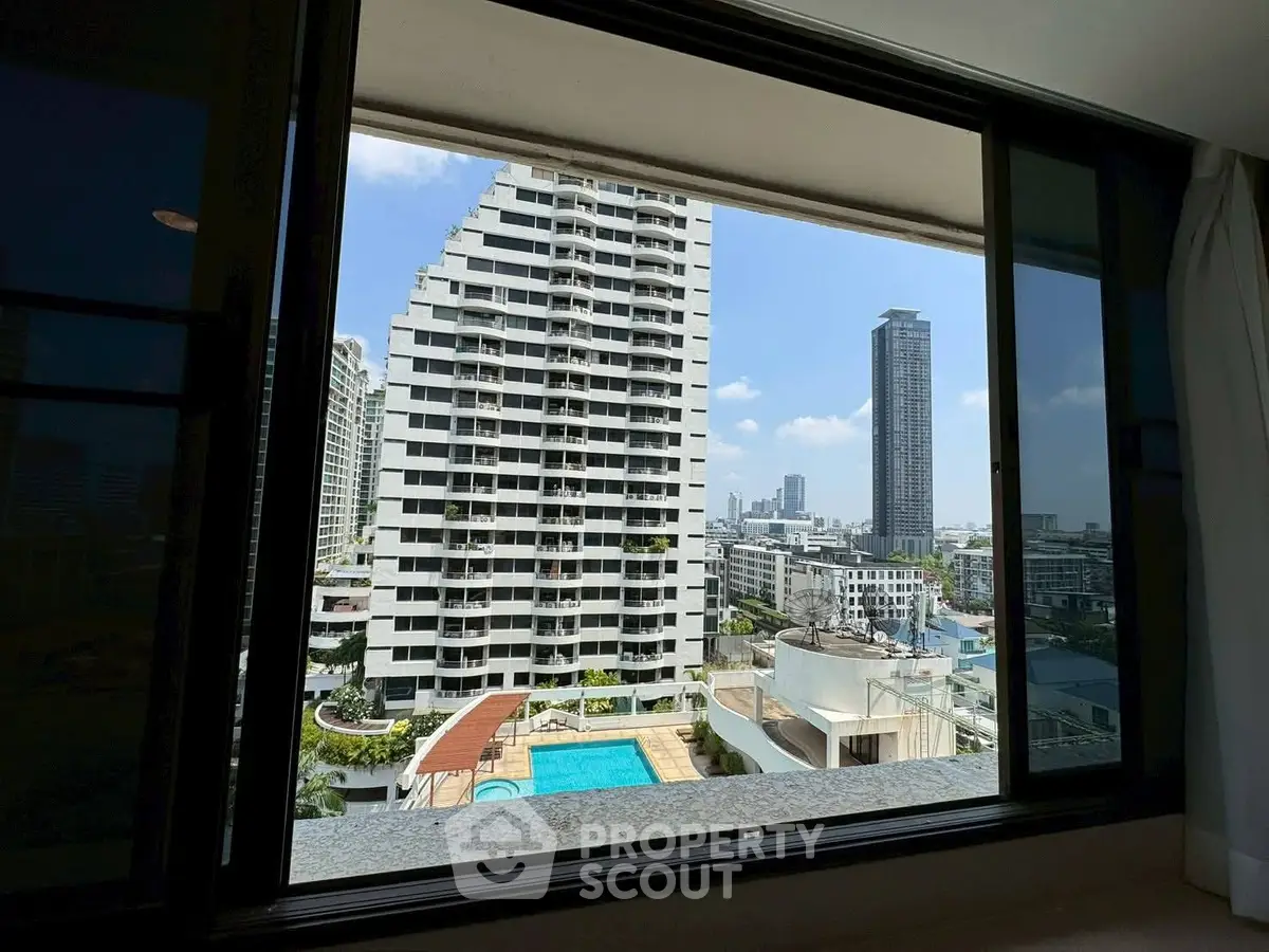 Stunning cityscape view from a high-rise apartment window overlooking a pool and modern buildings.