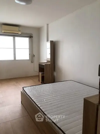 Minimalist bedroom with natural light and wooden flooring, featuring a bed and study desk.