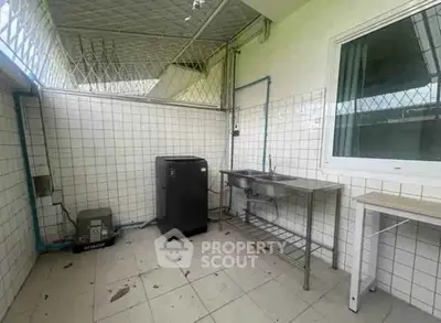 Outdoor laundry area with washing machine and sink in tiled space.