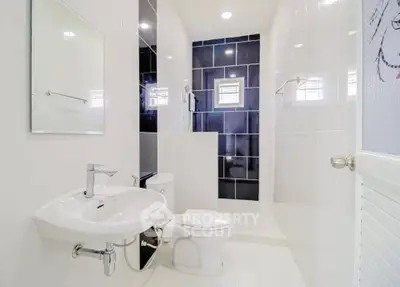 Modern white bathroom with sleek fixtures and black accent tiles.