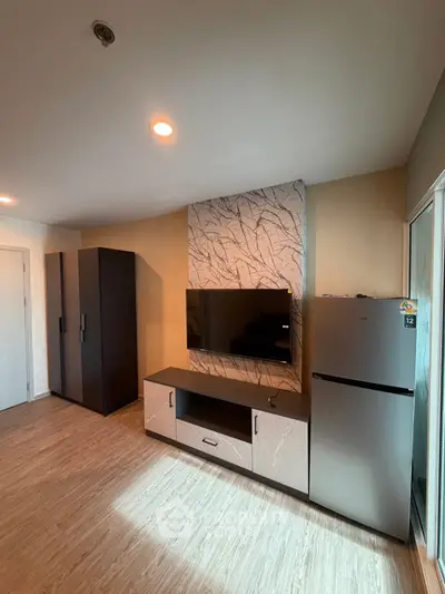 Modern living room with sleek TV unit and refrigerator, featuring stylish decor and ample storage space.