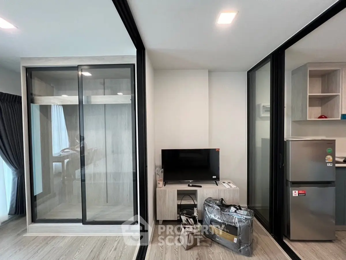 Modern apartment interior with sliding glass doors, TV, and stainless steel fridge, showcasing sleek design.