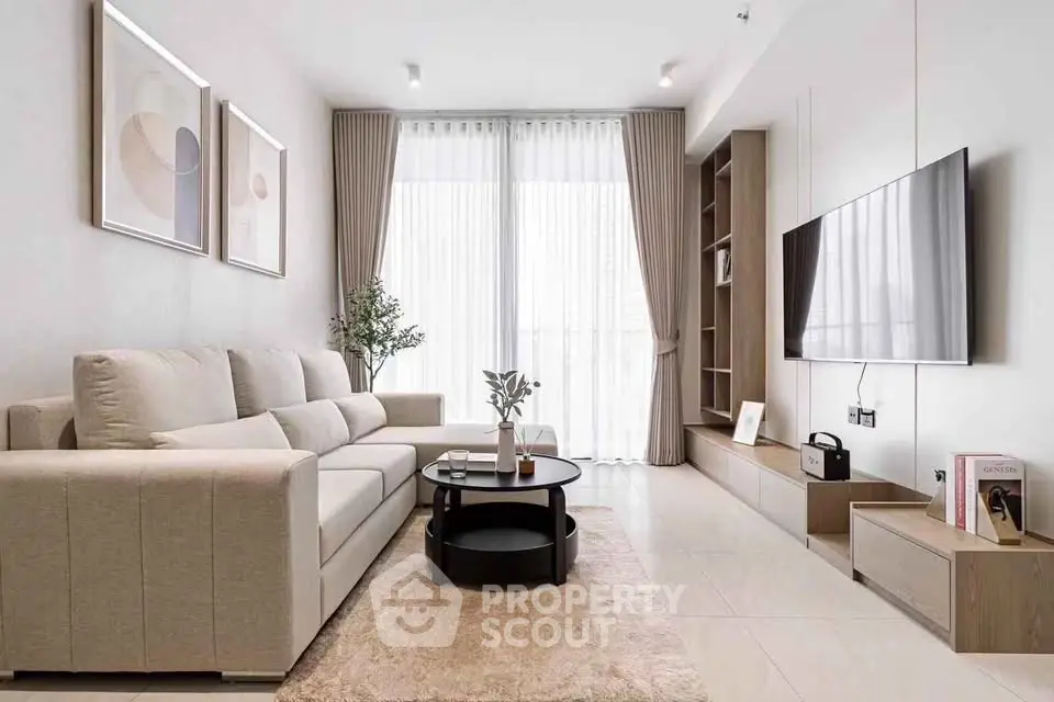 Elegant modern living room with large sofa, wall-mounted TV, and floor-to-ceiling windows.
