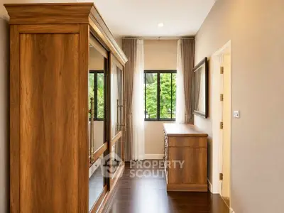 Elegant bedroom with wooden wardrobe and dresser, featuring large windows and natural light.