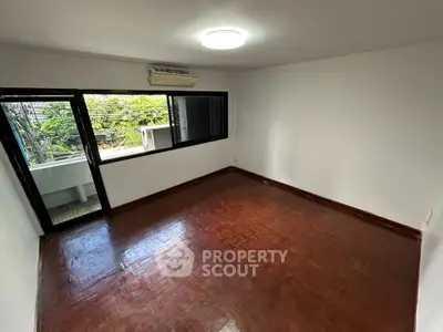 Spacious empty room with wooden flooring and large window offering natural light.