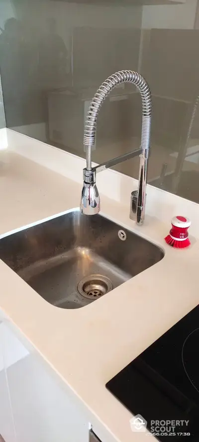 Sleek modern kitchen with stainless steel sink and high-arc faucet, complemented by a pristine white countertop and chic backsplash.