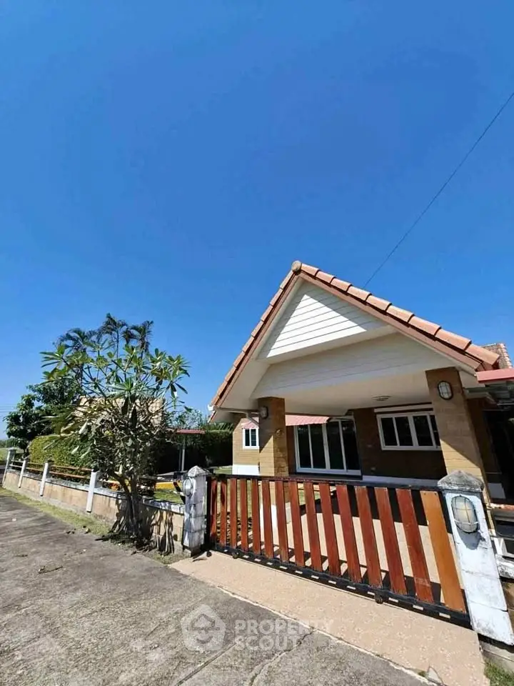Charming single-story house with a tiled roof and spacious front yard under a clear blue sky.