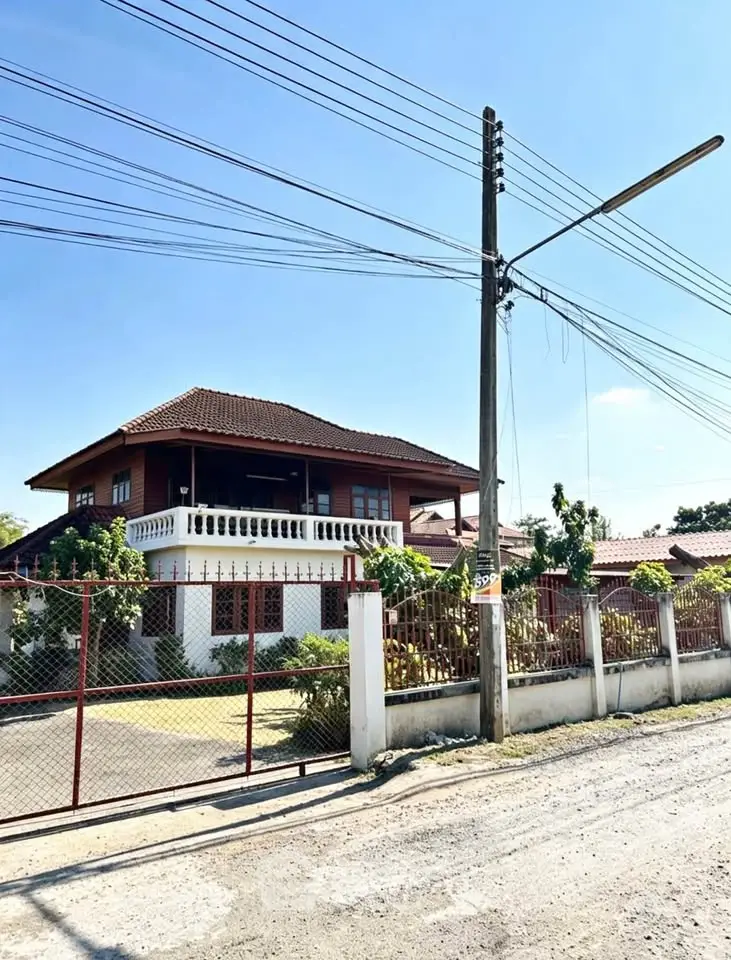 Charming two-story house with traditional design and spacious balcony, surrounded by lush greenery and secure fencing.