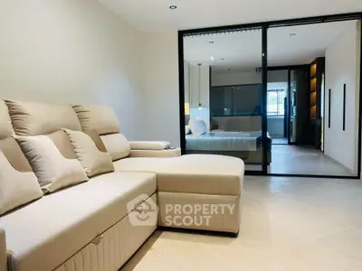Modern living room with beige sectional sofa and sliding glass doors leading to a stylish bedroom.