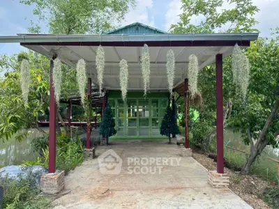Charming green house with covered patio surrounded by lush greenery and serene water view.