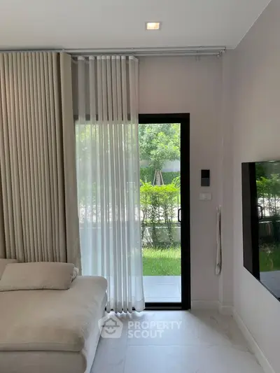 Modern living room with large window and garden view, featuring elegant curtains and a cozy sofa.