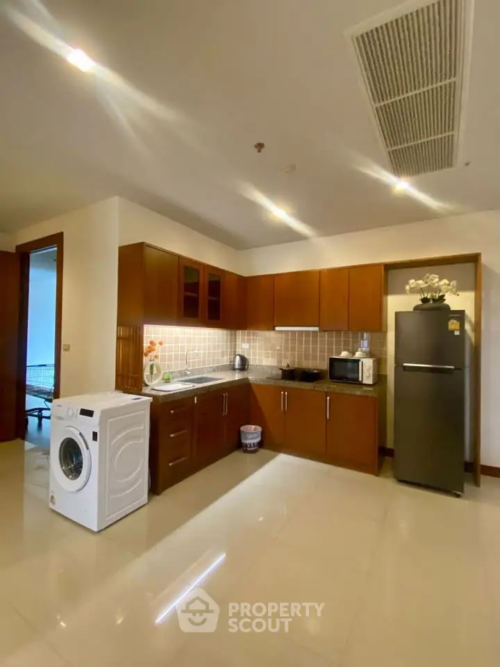 Modern kitchen with wooden cabinets, washing machine, and stainless steel fridge.