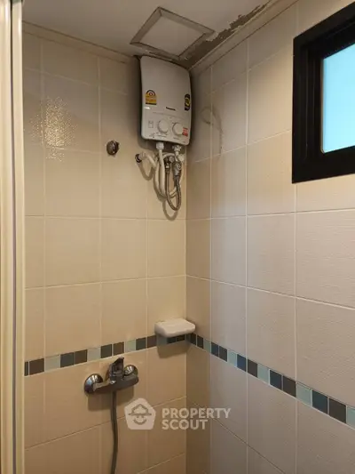 Compact bathroom with tiled walls and water heater, ideal for efficient space use.