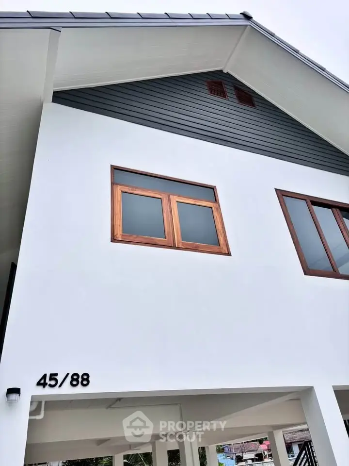 Modern white house exterior with wooden window frames and sloped roof design.