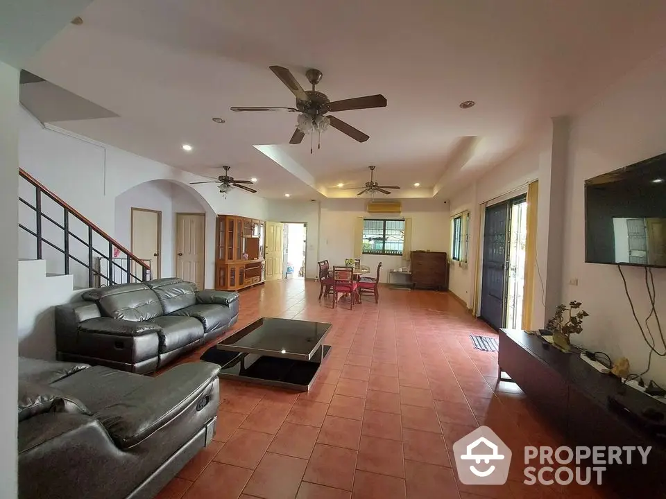 Spacious living room with terracotta tiled flooring, leather couches, and ample natural light, leading to an inviting dining area.