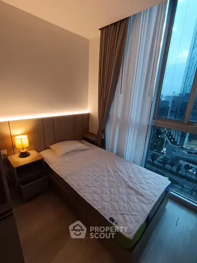 Modern bedroom with large window and city view, featuring cozy lighting and sleek design.