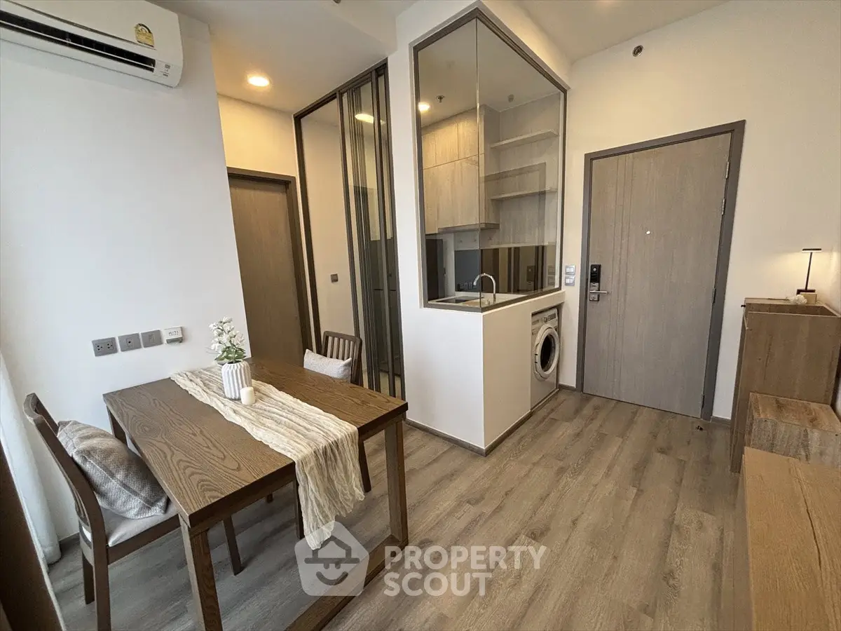 Modern apartment interior with dining area and compact kitchen featuring washing machine.