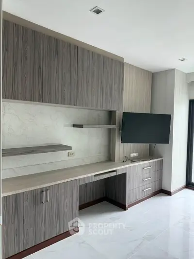Modern study room with built-in wooden desk and wall-mounted TV in a bright apartment.